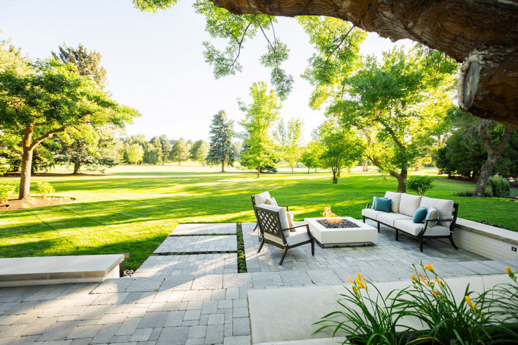 breathtaking sunlit backyard of property. foreground two chairs on brick surround an elegant fireplace